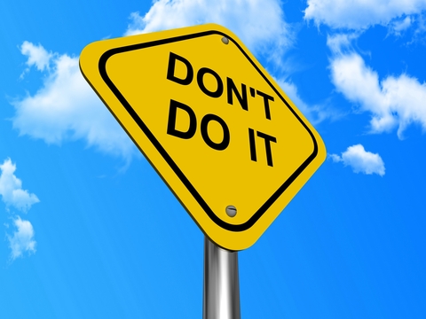 Diamond-shaped yellow street sign with black letters reading "DON'T DO IT" against a background of blue sky and clouds.